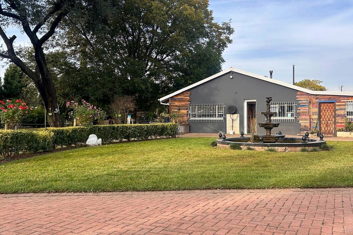 A well-maintained rear exterior view featuring a landscaped garden, a decorative water fountain, and a paved driveway leading to the main structure.