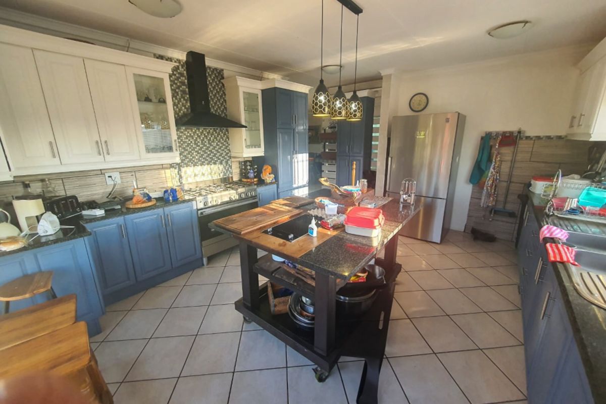 Spacious kitchen featuring a central island with granite countertops, gas stove, extractor fan, and ample built-in cabinetry with a mix of white and blue finishes.