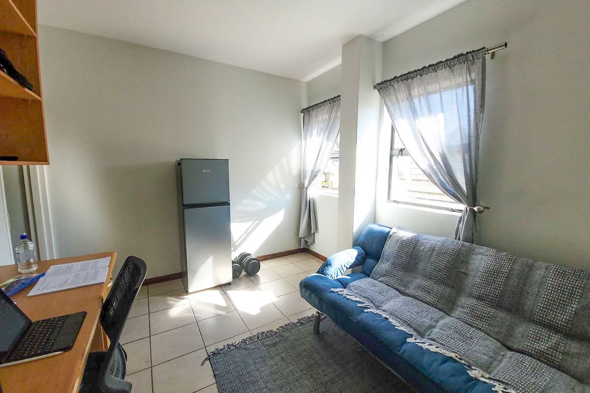 A functional living area featuring tiled flooring, neutral wall tones, and natural light through dual windows with installed curtain rods.