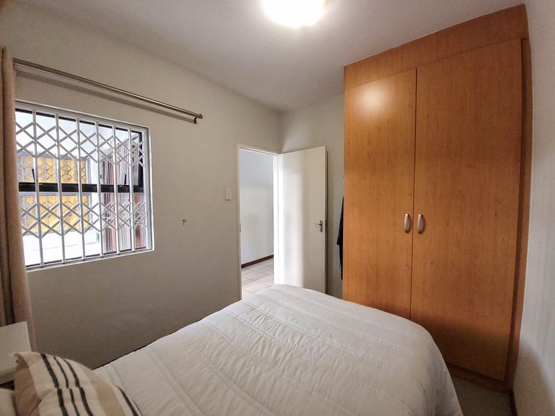 A bedroom featuring a built-in wooden wardrobe and a window fitted with a security gate.