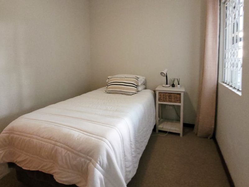 A compact bedroom featuring neutral walls, carpeted flooring, and a window fitted with a security gate.