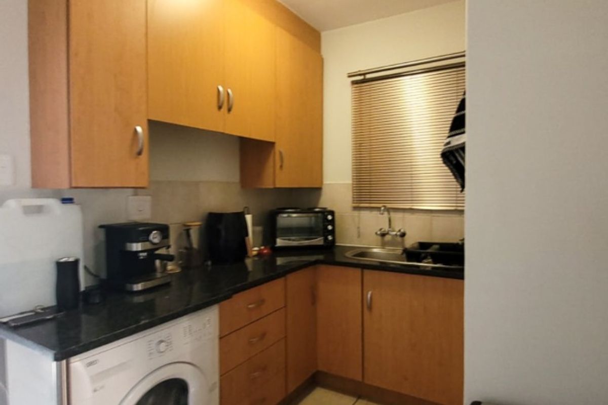 Compact kitchen featuring light wood cabinetry, granite countertops, tiled flooring, and integrated space for a washing machine.