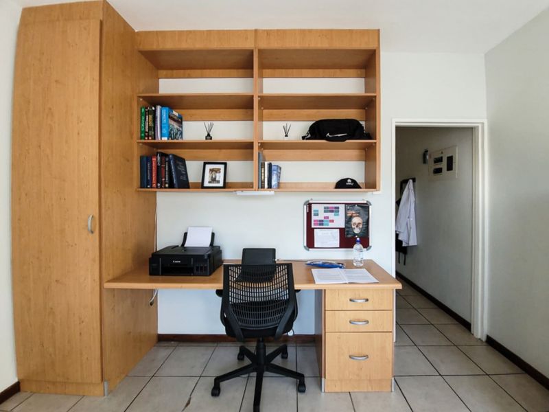 A functional home office space featuring built-in wooden cabinetry, shelving, and a desk, complemented by durable tiled flooring.