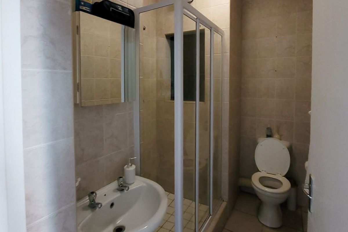 A compact bathroom featuring a pedestal basin, a shower enclosure, and a toilet, finished with neutral wall and floor tiling.