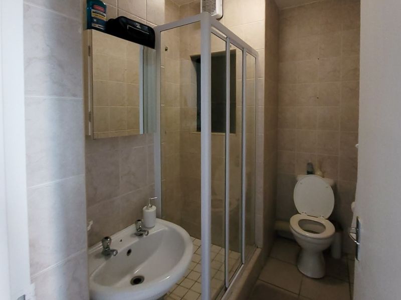 A compact bathroom featuring a pedestal basin, a shower enclosure, and a toilet, finished with neutral wall and floor tiling.
