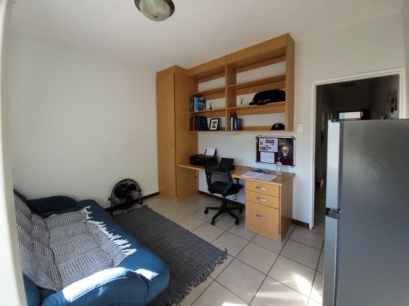 A functional home office space featuring built-in wooden desk, shelving, and cupboard storage with tiled flooring.