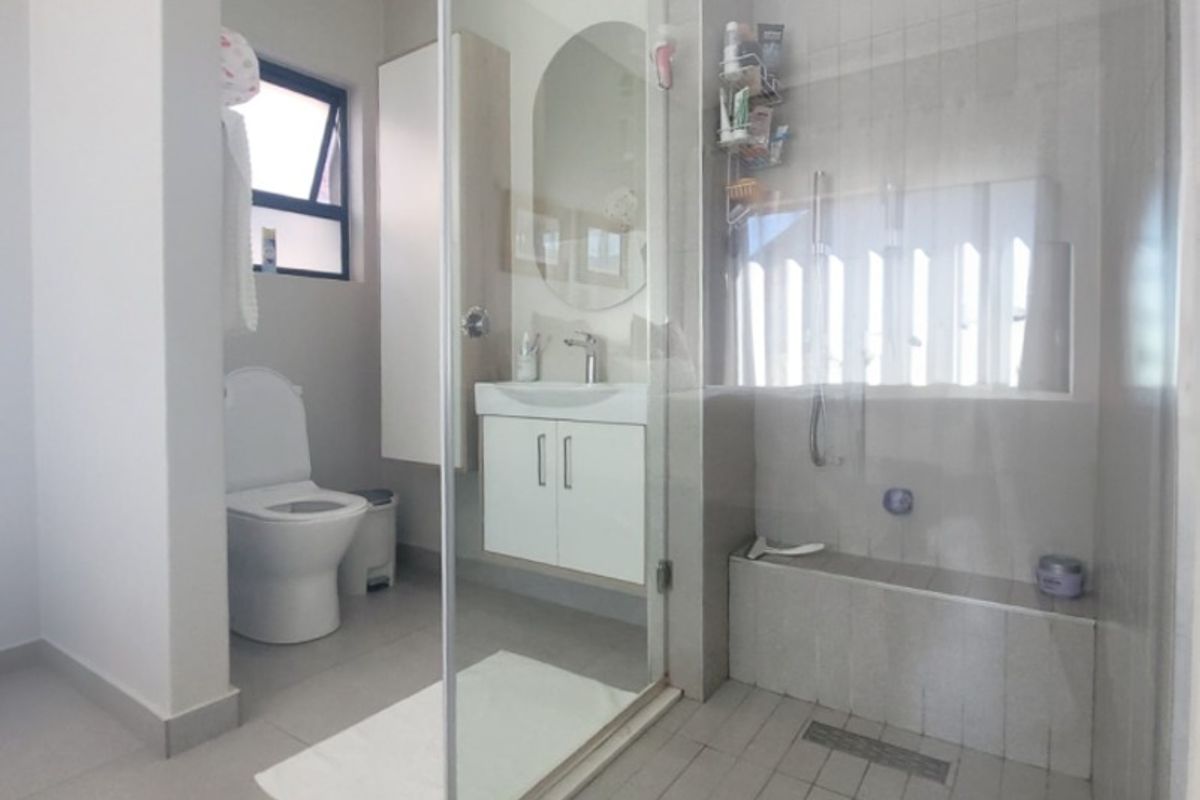 Modern bathroom featuring a spacious walk-in shower with glass screen, wall-mounted vanity, and neutral floor tiling.
