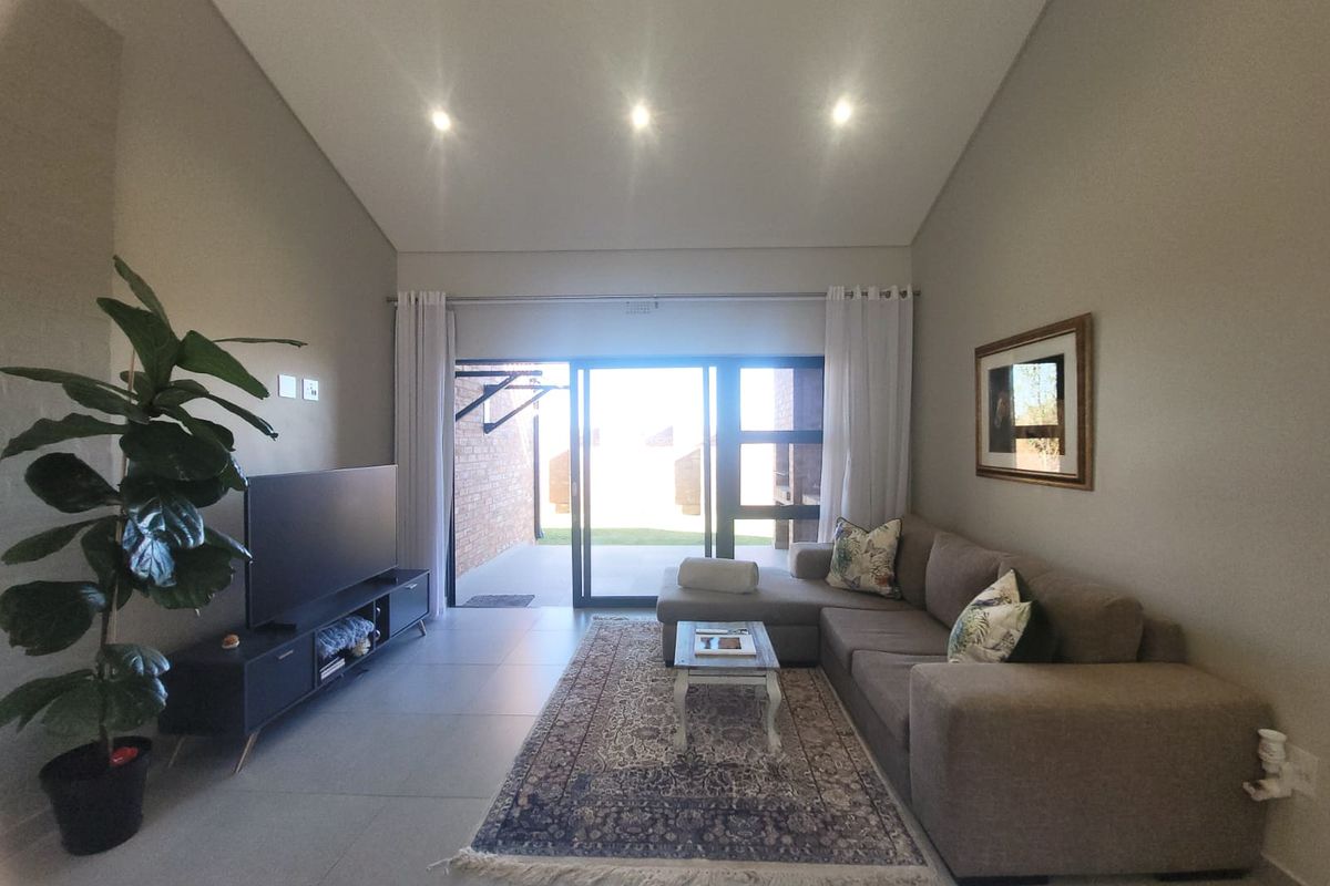A bright living room featuring a vaulted ceiling, recessed downlights, tiled flooring, and a large sliding glass door providing access to the outdoor area.