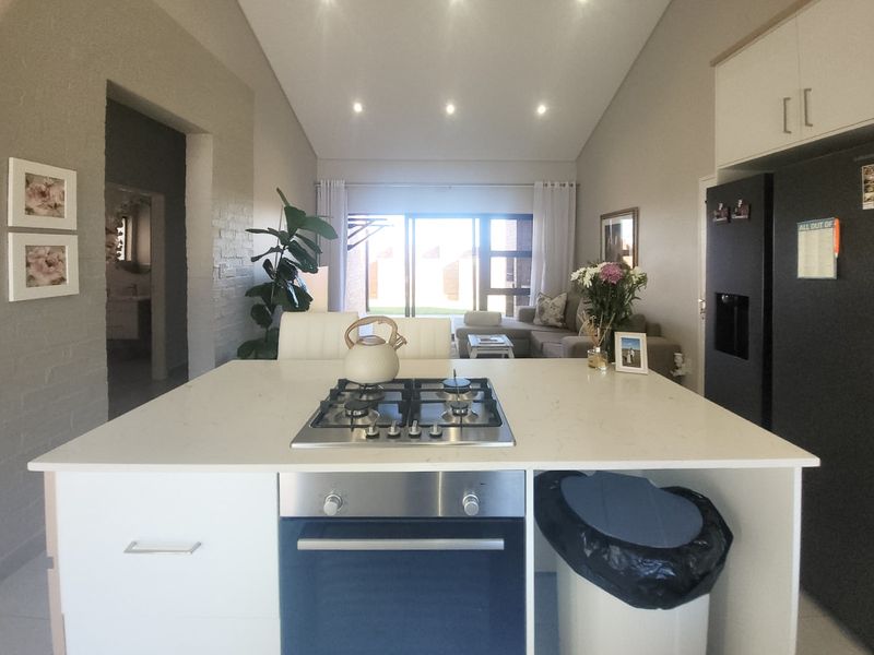 Open-plan living area featuring a central kitchen island with gas hob and oven, vaulted ceilings, and sliding doors leading to the exterior.