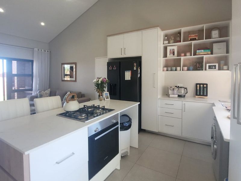 Modern open-plan kitchen featuring a central island with gas cooktop, built-in oven, ample cabinetry, and high vaulted ceilings with recessed lighting.