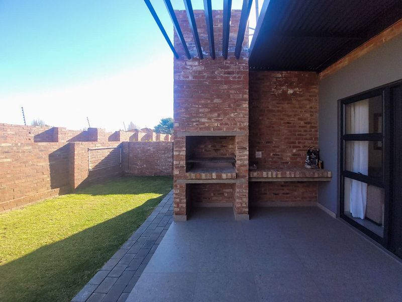 A covered outdoor patio featuring a built-in brick braai, tiled flooring, and direct access to a private garden area with brick boundary walls.