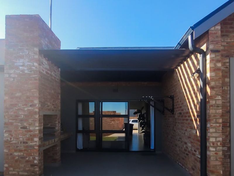 A covered patio area featuring a built-in brick braai, exposed brickwork, and sliding glass doors providing access to the interior living space.