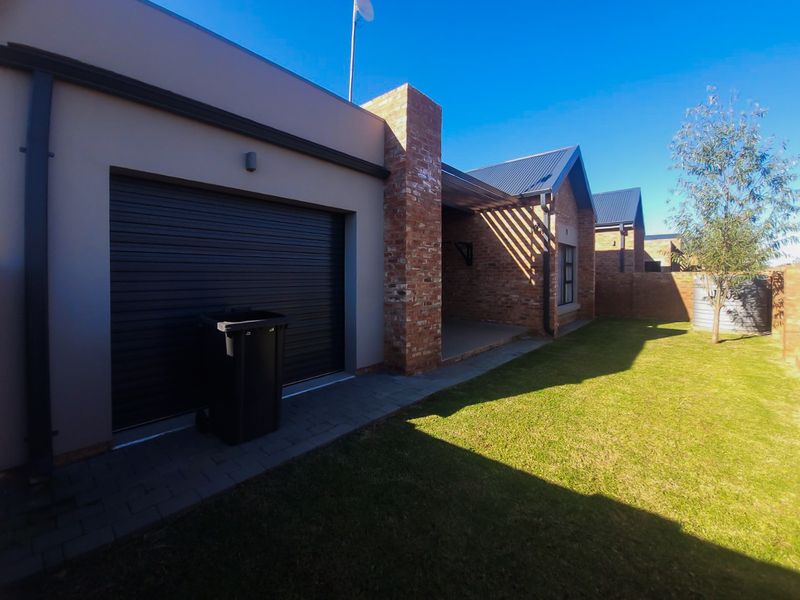 Rear view of the townhouse featuring a roller garage door, brick architectural detailing, a covered patio area, and a private garden with a rainwater tank.