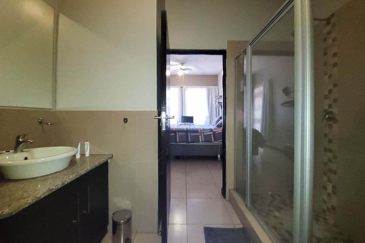 A functional bathroom featuring a vanity with a countertop basin, a large wall mirror, and a glass-enclosed shower with tiled finishes.