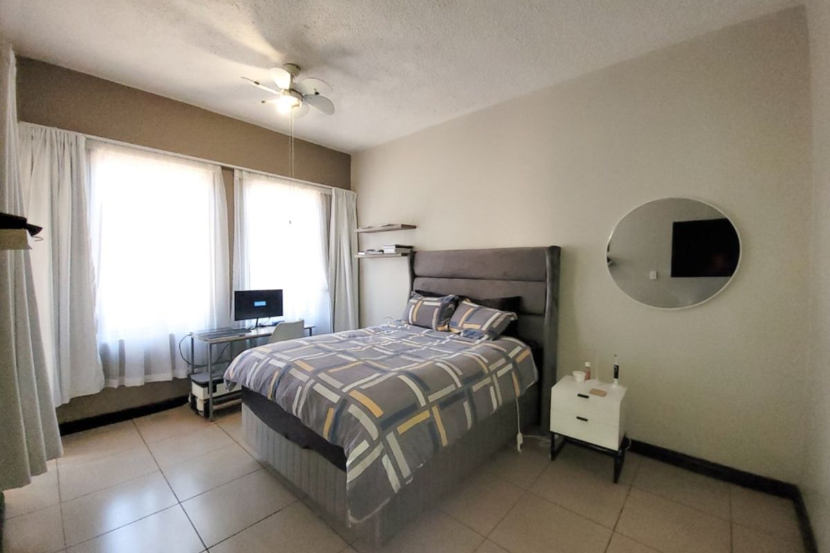 A bedroom featuring tiled flooring, a ceiling fan, and built-in shelving, offering a functional space with neutral finishes.