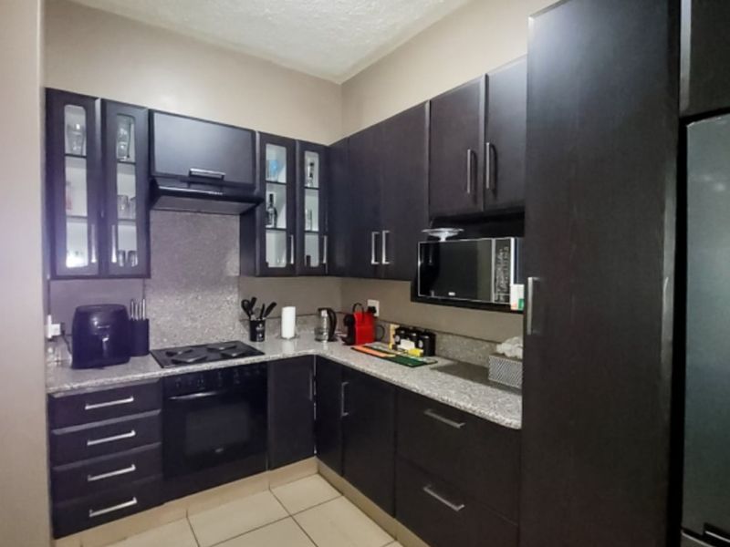 A compact, functional kitchen featuring dark wood cabinetry, granite countertops, and integrated appliances including a gas hob, oven, and built-in microwave.