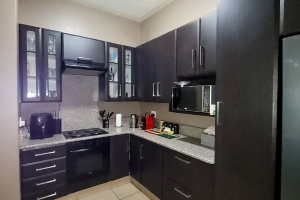 A compact, functional kitchen featuring dark wood cabinetry, granite countertops, and integrated appliances including a gas hob, oven, and built-in microwave.