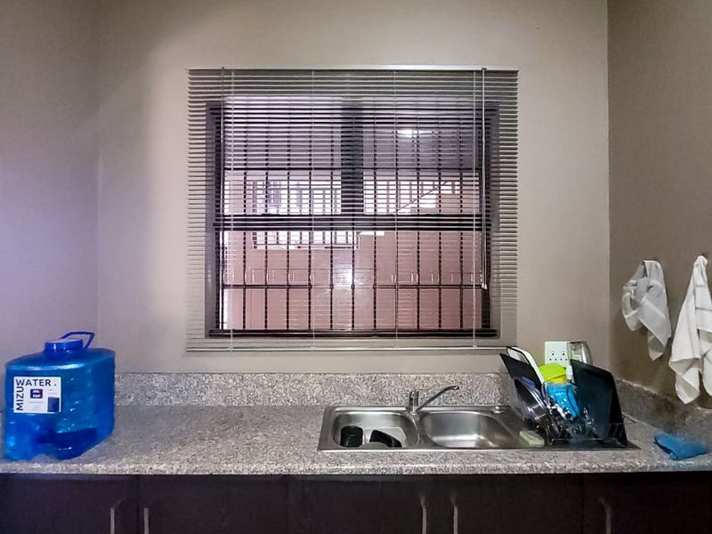 A functional kitchen area featuring dark wood cabinetry, a granite countertop, and a double basin stainless steel sink with a window view.