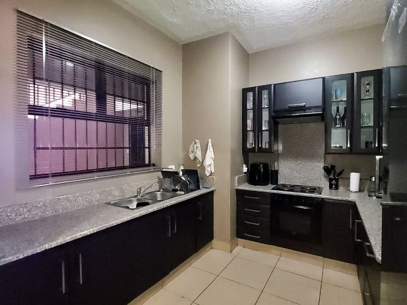 A functional kitchen featuring dark cabinetry, granite countertops, built-in oven and hob, and tiled flooring with security bars on the window.