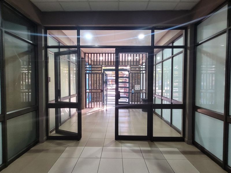 A bright and clean apartment building entrance lobby featuring tiled flooring, glass-paneled doors, and a secure metal gate.
