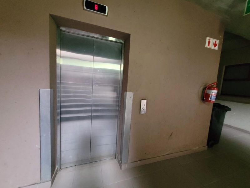 A functional apartment building elevator lobby area featuring stainless steel elevator doors, tiled flooring, and wall-mounted fire safety equipment.