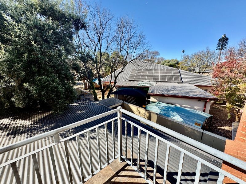An elevated balcony with a metal balustrade overlooking the rear property area, featuring views of neighboring rooftops and mature trees.
