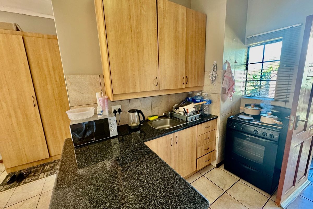 Compact kitchen featuring granite countertops, light wood-finish cabinetry, tiled backsplash, and a freestanding stove, providing a functional workspace.
