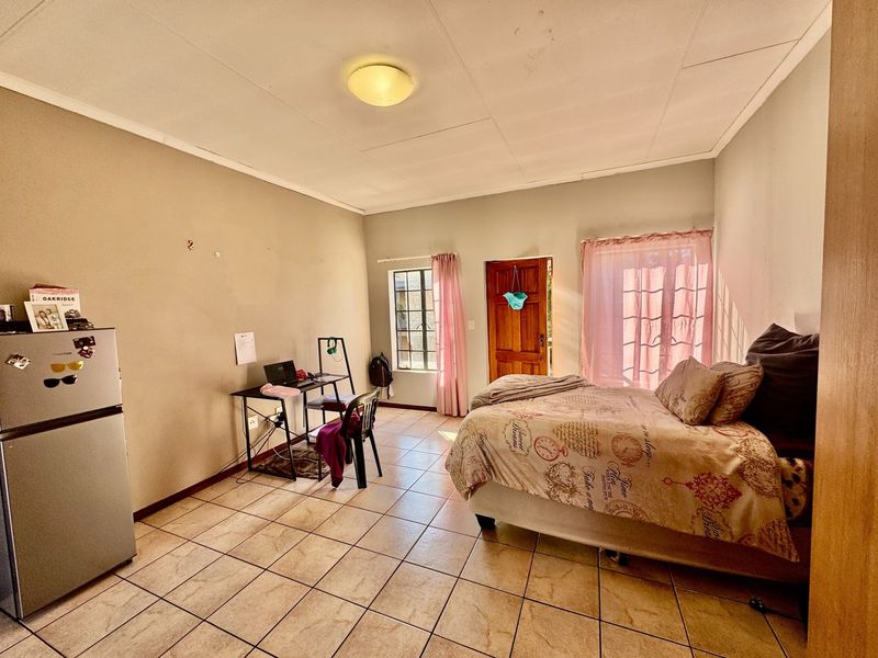A bedroom featuring tiled flooring, a timber door, and natural light through the window. The space requires cosmetic updates to improve its overall condition.