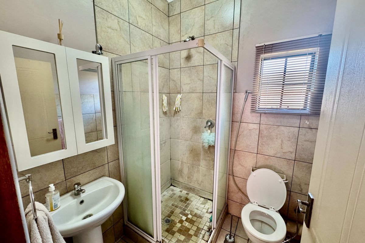 A functional bathroom featuring a pedestal basin, a corner shower enclosure, and a toilet, finished with neutral wall and floor tiling.