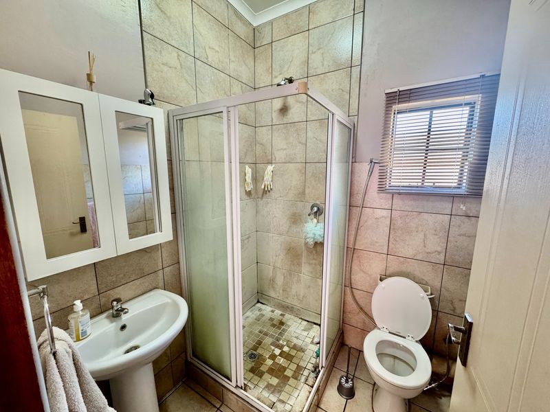 A functional bathroom featuring a pedestal basin, a corner shower enclosure, and a toilet, finished with neutral wall and floor tiling.