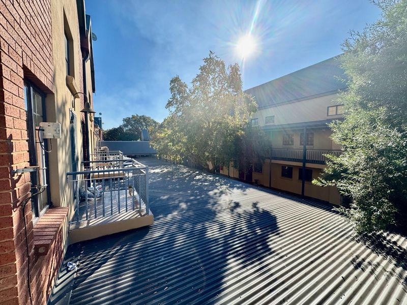 An elevated view of a balcony area featuring a metal balustrade and overlooking a corrugated metal roof structure within an apartment complex.