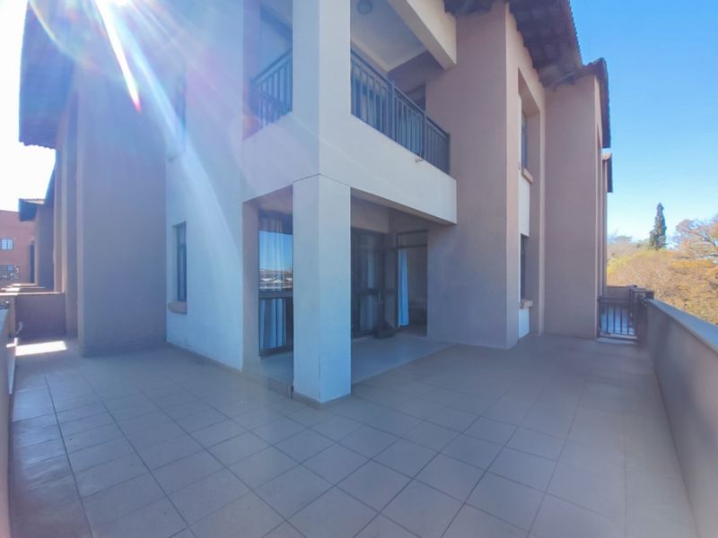 A spacious covered balcony featuring tiled flooring and metal balustrades, providing an outdoor extension to the apartment living area.