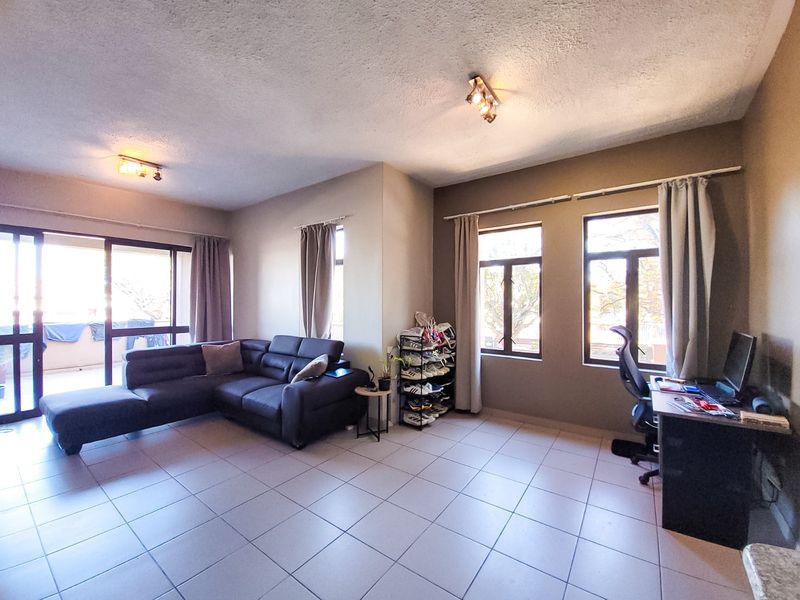 Spacious open-plan living area featuring tiled flooring, large windows for natural light, and direct access to an outdoor balcony through sliding glass doors.