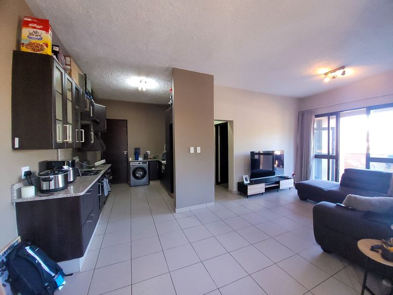 Open-plan living area featuring a kitchen with dark cabinetry and granite countertops, tiled flooring throughout, and direct access to a balcony.