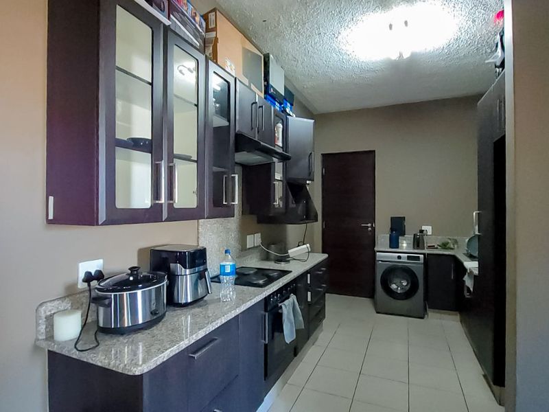 A functional kitchen featuring dark cabinetry, granite countertops, built-in oven and hob, and integrated laundry space with tiled flooring throughout.