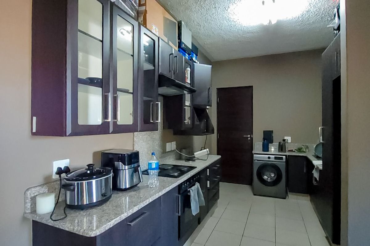 A functional kitchen featuring dark cabinetry, granite countertops, built-in oven and hob, and integrated laundry space with tiled flooring throughout.