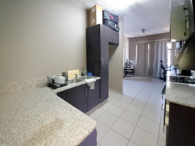 Open-plan kitchen and living area featuring dark built-in cabinetry, laminate countertops, a double basin sink, and tiled flooring throughout.