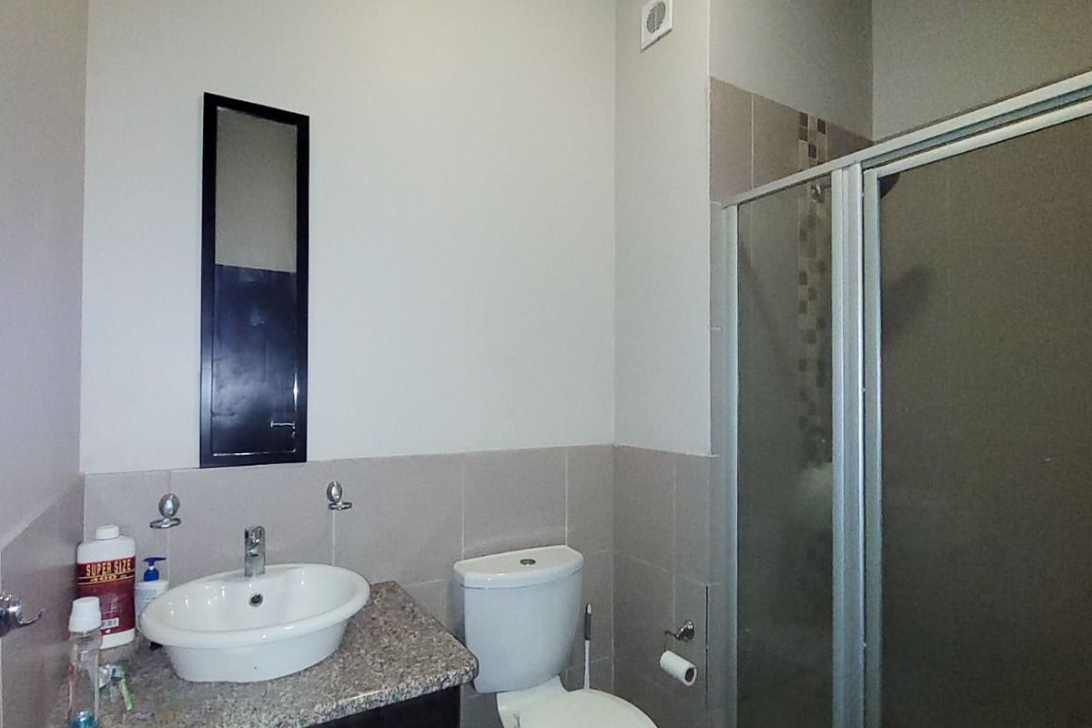 A functional bathroom featuring a vanity with granite countertop, ceramic basin, toilet, and a glass-enclosed shower with tiled splashback.