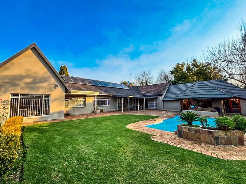 Rear view of the property featuring a swimming pool, brick paved patio area, and solar panels installed on the tiled roof.
