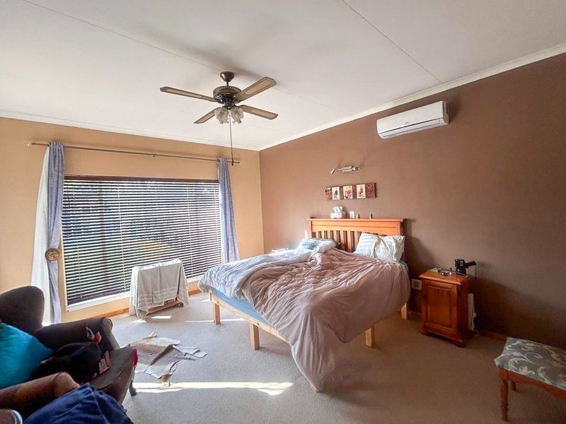 A spacious bedroom featuring a ceiling fan, split-system air conditioning unit, and large window with venetian blinds.