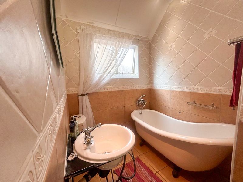 A compact bathroom featuring a classic freestanding bathtub, pedestal basin, and neutral ceramic wall tiling with decorative border accents.