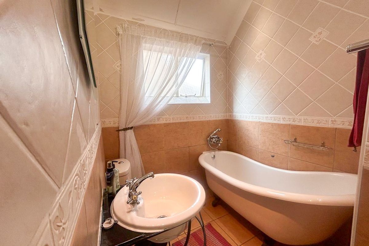 A compact bathroom featuring a classic freestanding bathtub, pedestal basin, and neutral ceramic wall tiling with decorative border accents.