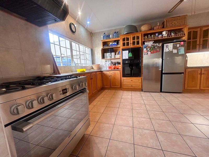 Spacious kitchen featuring wooden cabinetry, a gas stove with extractor fan, built-in oven, and tiled flooring throughout.