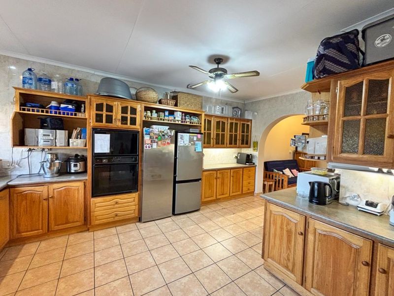 A functional kitchen featuring extensive wooden cabinetry, tiled flooring, a built-in oven, and a ceiling fan, offering ample storage and workspace.