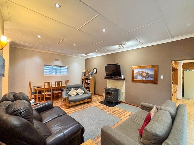 Open-plan living and dining area featuring a wood-burning stove with stone surround, recessed lighting, and laminate flooring.