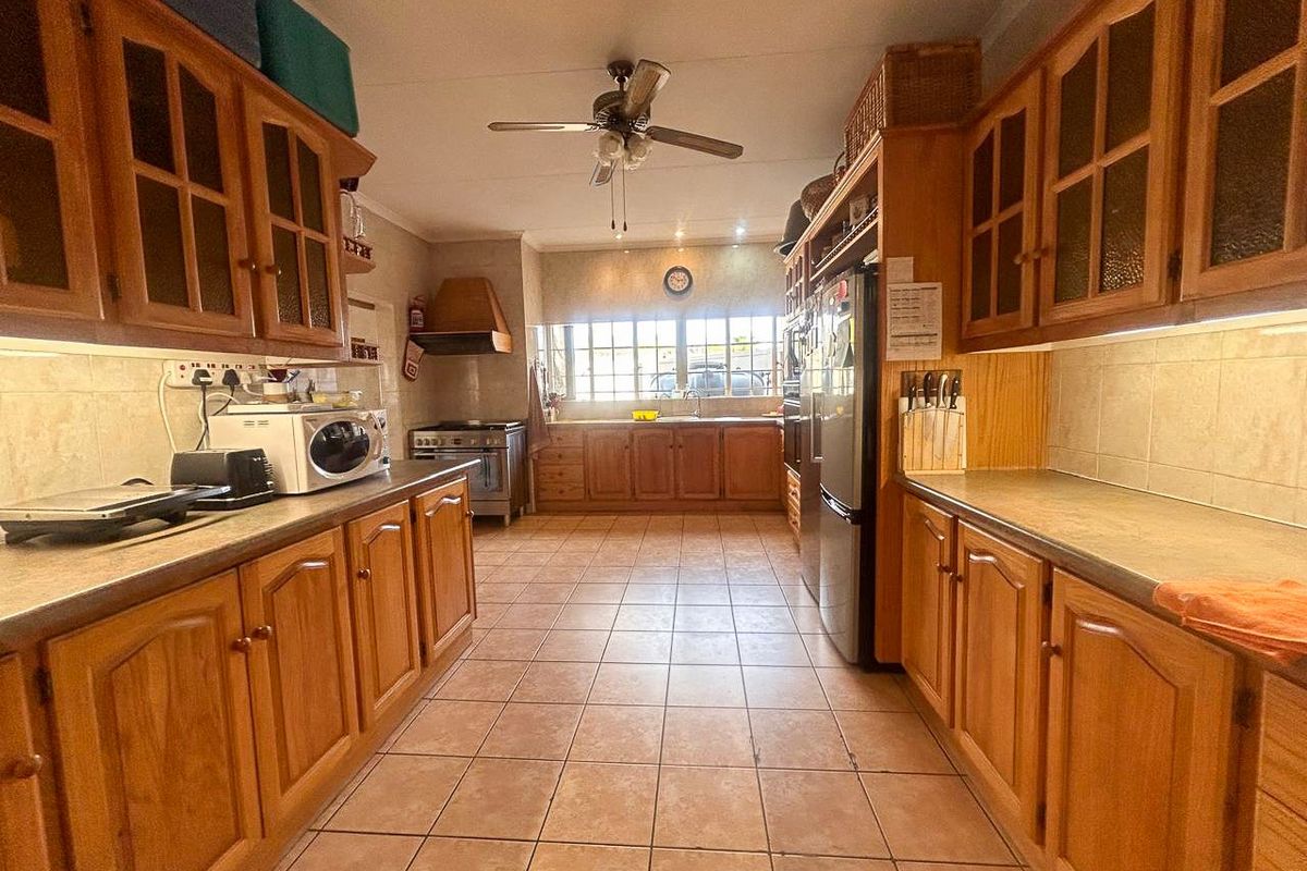 A spacious kitchen featuring extensive wooden cabinetry, tiled flooring, a built-in stove with extractor fan, and ample counter space for meal preparation.