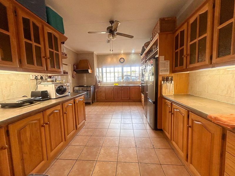 A spacious kitchen featuring extensive wooden cabinetry, tiled flooring, a built-in stove with extractor fan, and ample counter space for meal preparation.