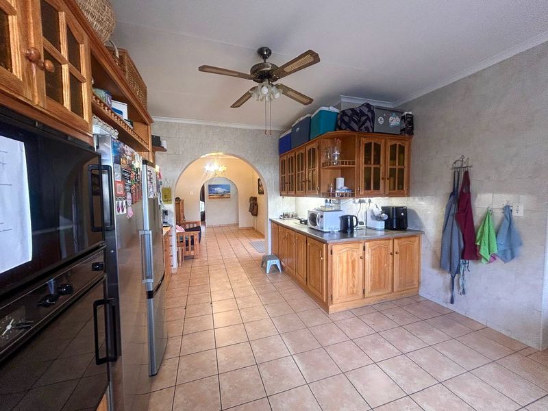 A functional kitchen featuring wooden cabinetry, tiled flooring, and a ceiling fan, with an open archway leading to the adjacent living area.