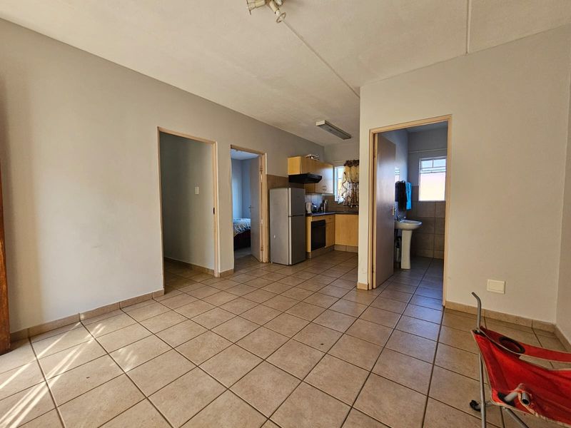 Open plan living area featuring tiled flooring, leading into a compact kitchen and bathroom space with basic built-in cabinetry and fixtures.