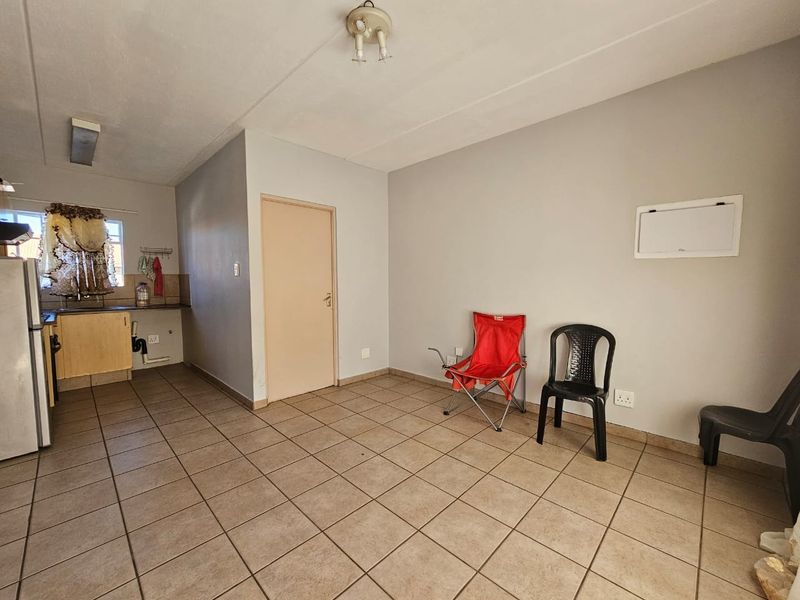 Open-plan living area featuring tiled flooring and a compact kitchen corner with built-in cabinetry and sink, offering a functional blank canvas.
